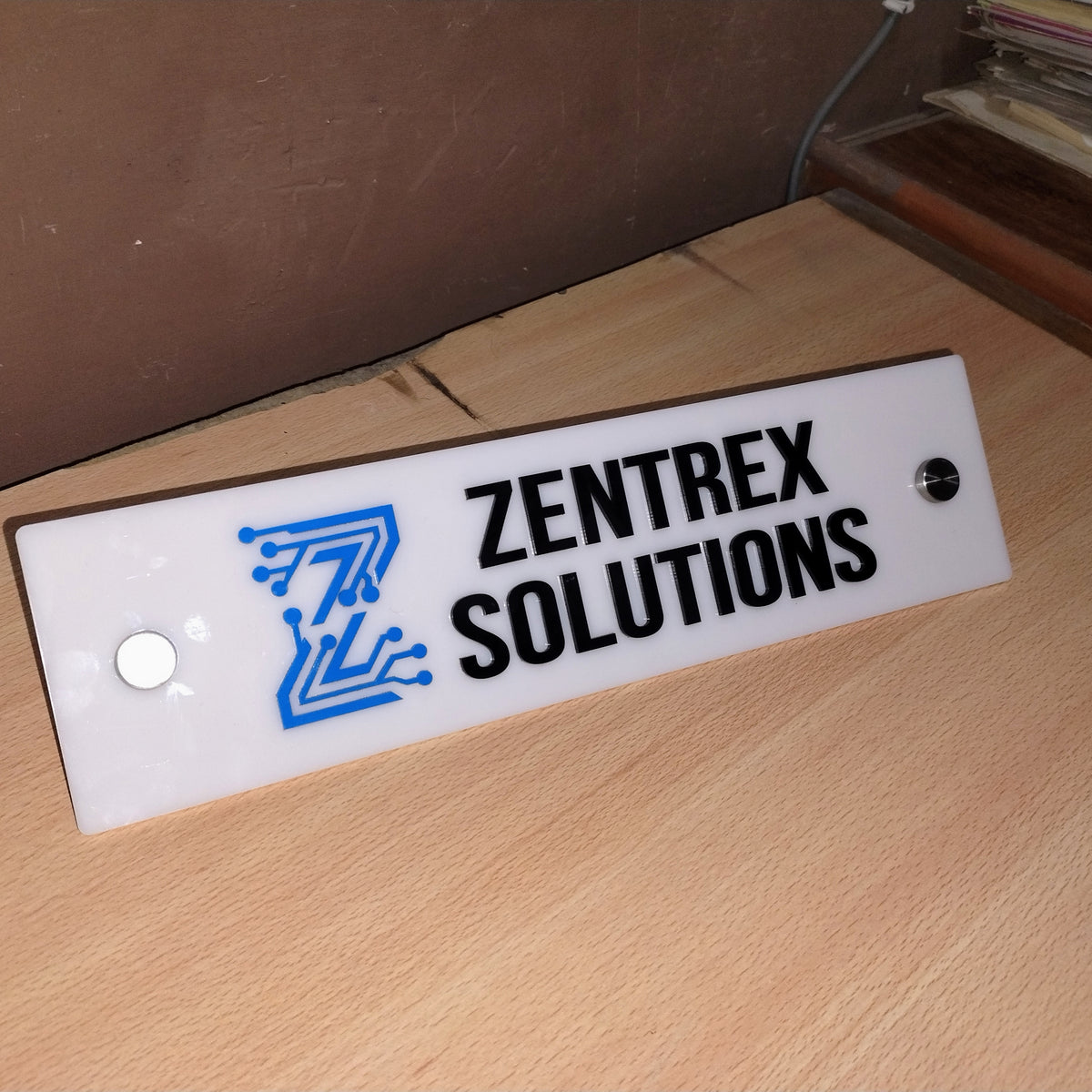 White acrylic office name plate with raised blue logo, black lettering and stainless steel mounts